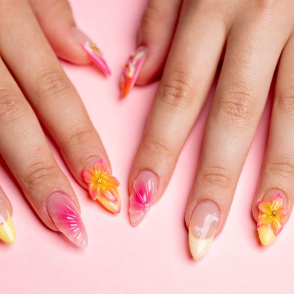 Mãos com press on nails nas unhas com nail art com flores e tons em rosa e amarelo de esmalte.