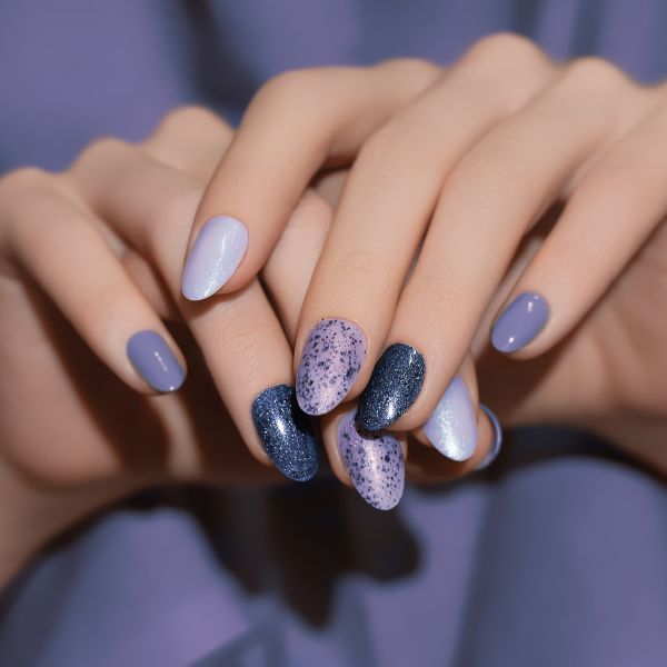Mão com unhas de diferentes cores e texturas de roxo e lilás.