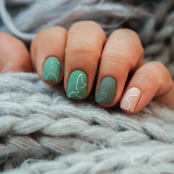 Uma mão com unhas curtas e quadradas em tom verde fosco com detalhes de linhas brancas.