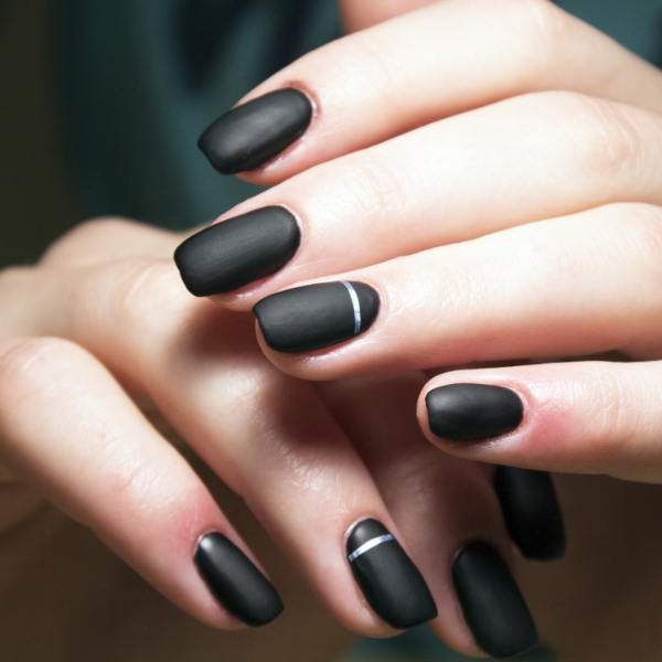Mãos de uma mulher branca com esmalte escuro de cor preta e acabamento fosco matte.