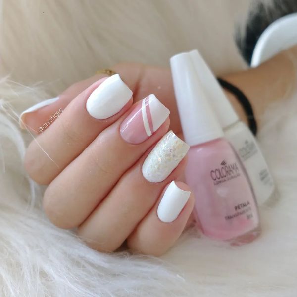 Foto de unhas feitas utilizando esmalte branco de diversos modos, com duas unhas lisas, uma com glitter grosso branco e uma com base nude e francesinha diagonal branca.