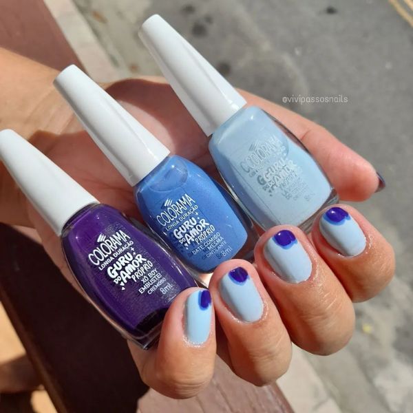 Foto de unhas feitas em tons de azul, onde todas as unhas possuem uma base azul clara e no canto superior direito foi feito uma bolinha em um tom mais intenso de azul com uma outra bolinha de um tom ainda mais escuro dentro.