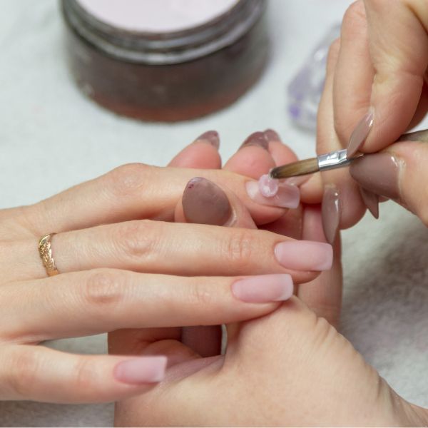 Profissional manicure aplica uma base fortalecedora nas unhas de sua cliente para prevenir manchas brancas nas unhas.
