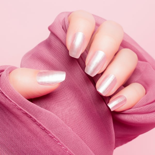 Mãos femininas com as unhas em formato longo e de cor rosa perolada.