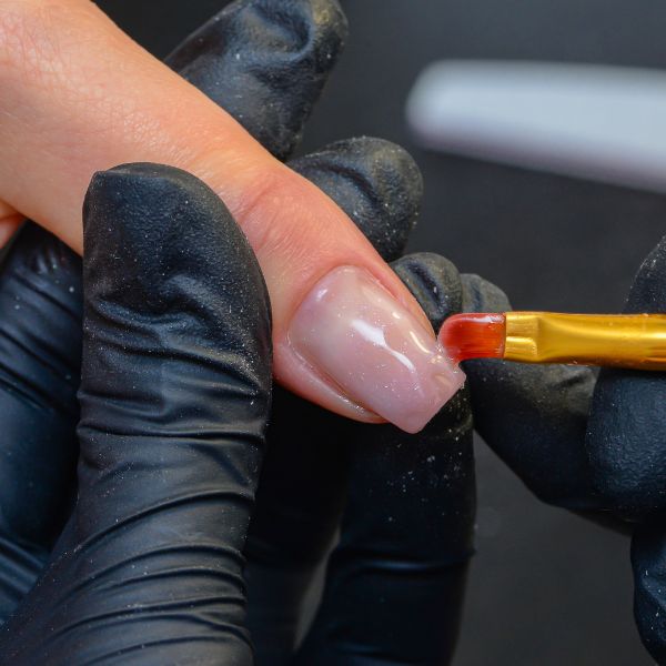 Manicure aplica um esmalte fortalecedor de unhas nas unhas de sua cliente para fortalecer e evitar as unhas quebradas.