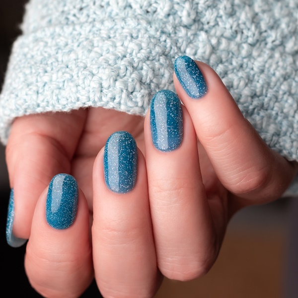 Modelo com unhas pintadas de azul com glitter
