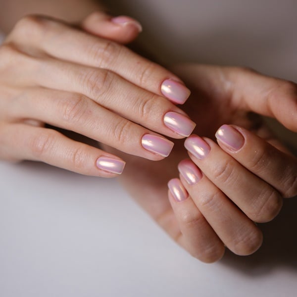 Unhas com esmalte perolado rosa claro.