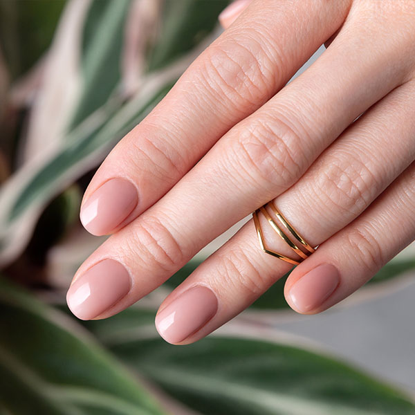 Mãos com unhas curtas pintadas de esmalte nude rosado, criando um visual elegante e natural