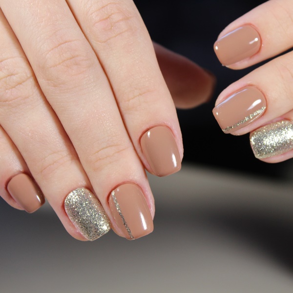 Mãos com esmalte bege na unha e glitter no dedo anelar.