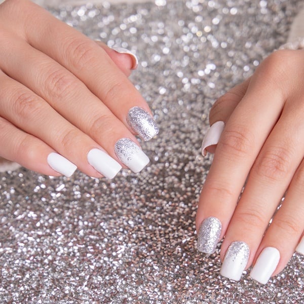 Mãos com unha branca com glitter para o fim do ano em fundo com glitter prateado.