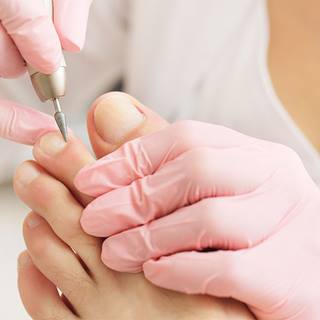 Profissional com luvas rosas realiza pedicure usando ferramenta elétrica no dedão do pé