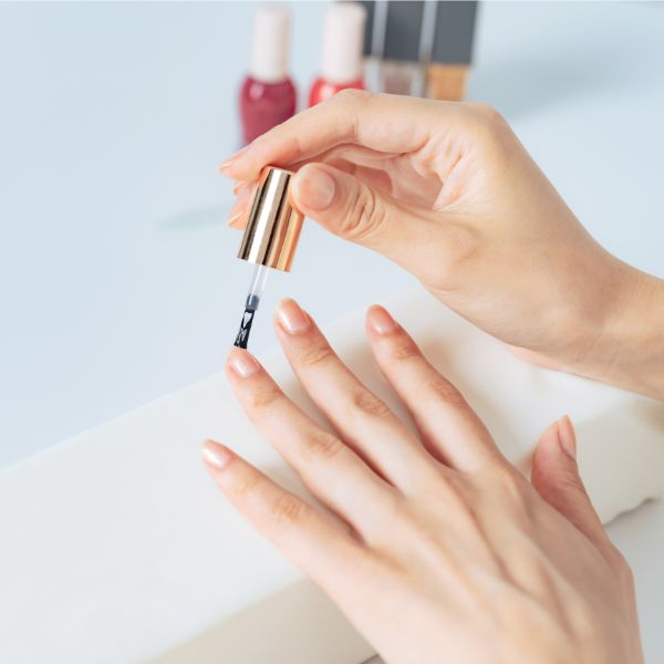Mulher aplicando base de unha em suas unhas naturais.