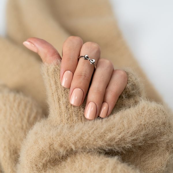 Mão com manga de casaco felpudo bege e unhas clean em tom nude perolado.jpg