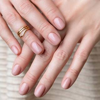 Unha minimalista curta em tom nude e anel dourado no dedo anelar.