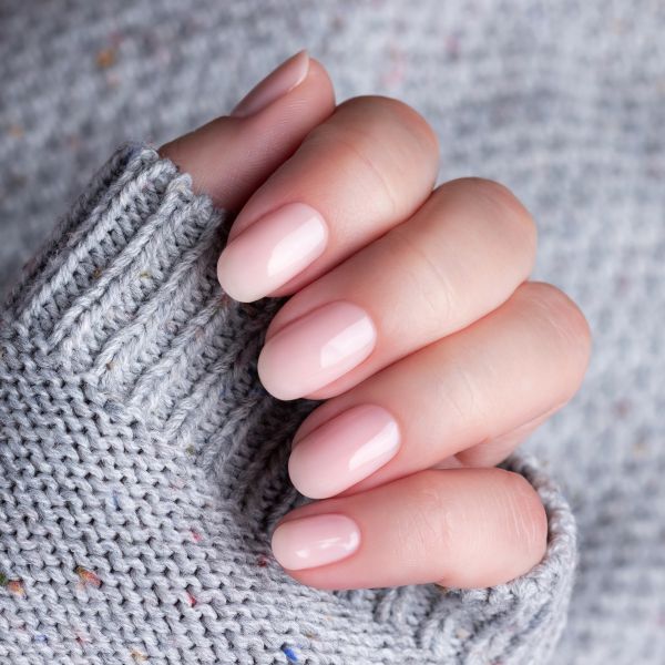 Mão com casaco cinza e unhas clean em tom nude.