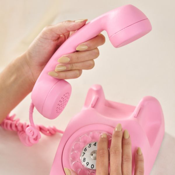 Mão em telefone fixo rosa pastel com Esmalte Areia da Coleção Colorama Retrô.
