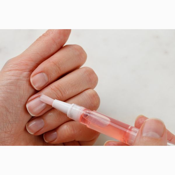 Mulher passando canetinha hidratante de cutícula nas unhas.