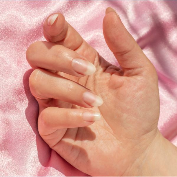 Mão com unhas longas em fundo rosa.