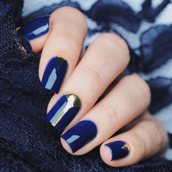 Unhas azul escuro com nail art dourada.