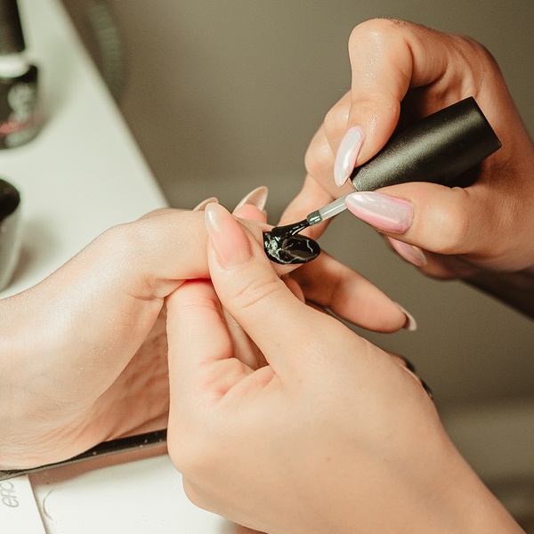 Manicure pintando a unha de sua cliente com esmalte preto.