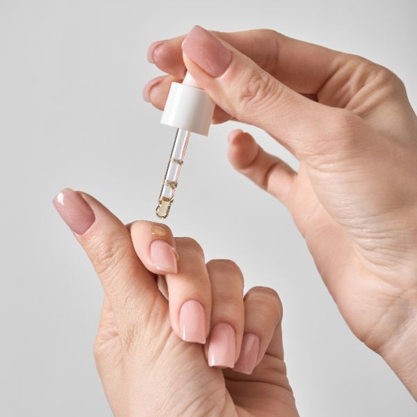 Mulher aplicando secante de unha em conta gotas em suas unhas com esmalte nude claro.