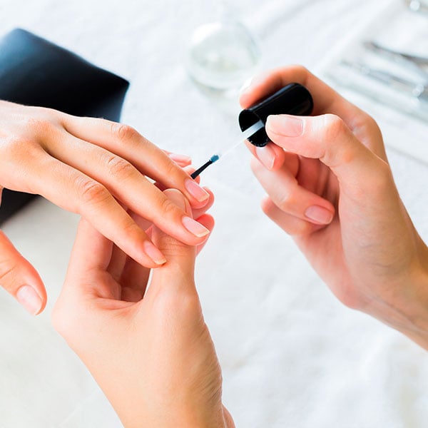 Manicure passando secante de esmalte na unha da cliente