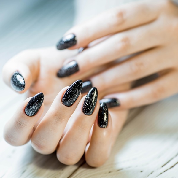 Mão com unhas pretas encapsuladas com glitter prateado.