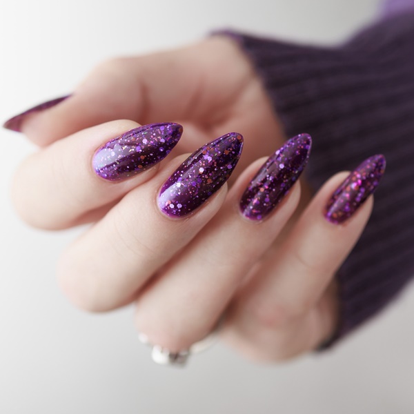 Mão com unha com glitter roxo.
