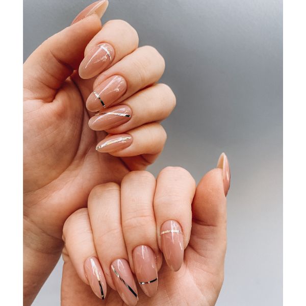 Mão com nail art em suas unhas simples com tom nude de base e linhas em dourado.