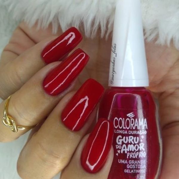 Foto de unhas com esmaltação vermelho cereja segurando o esmalte Colorama utilizado.