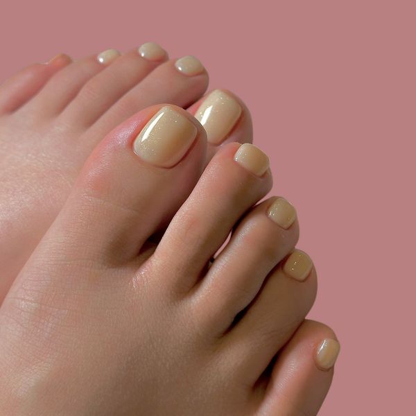 Decoração de unha do pé com esmalte bege claro, em um fundo rosa.