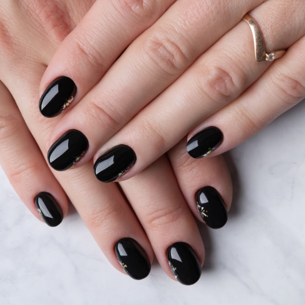 Mãos de uma mulher com as unhas decoradas com esmalte preto em tom cintilante.