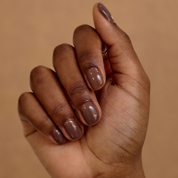 Mão direita de uma mulher negra com as unhas decoradas com esmalte marrom escuro.