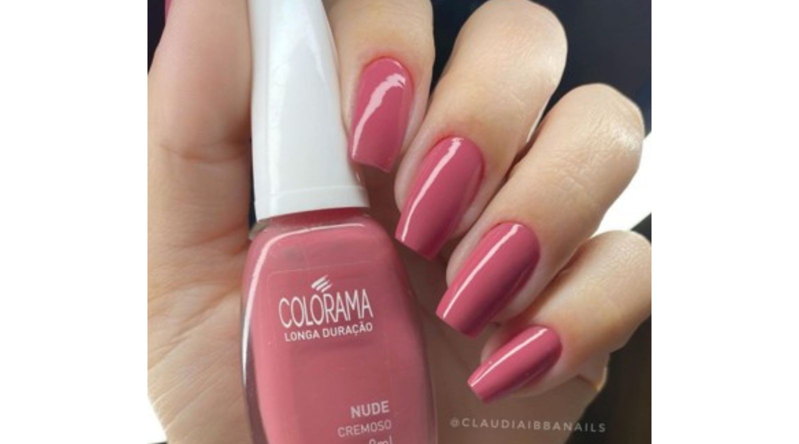 Mão segurando esmalte Colorama Longa Duração Nude Cremoso com unhas longas quadradas em tom rosa nude brilhante ao fundo escuro.