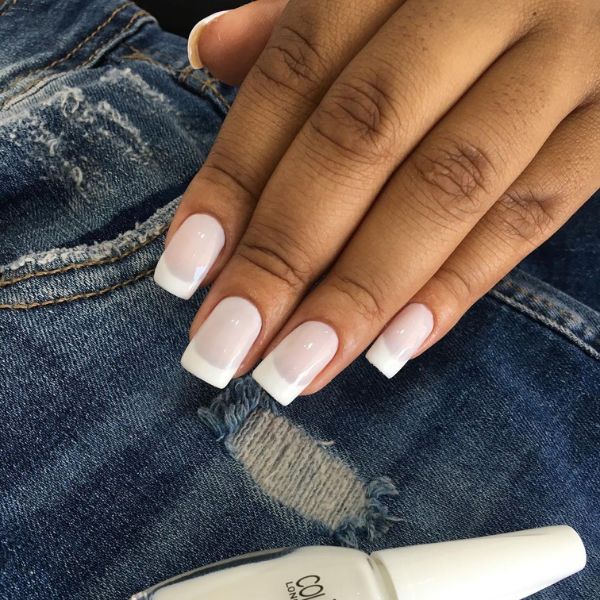 Foto de unhas feitas com base rosa claro e detalhes de francesinha em todos os dedos, com um tecido jeans ao fundo e o vidro de esmalte utilizado logo abaixo da mão.