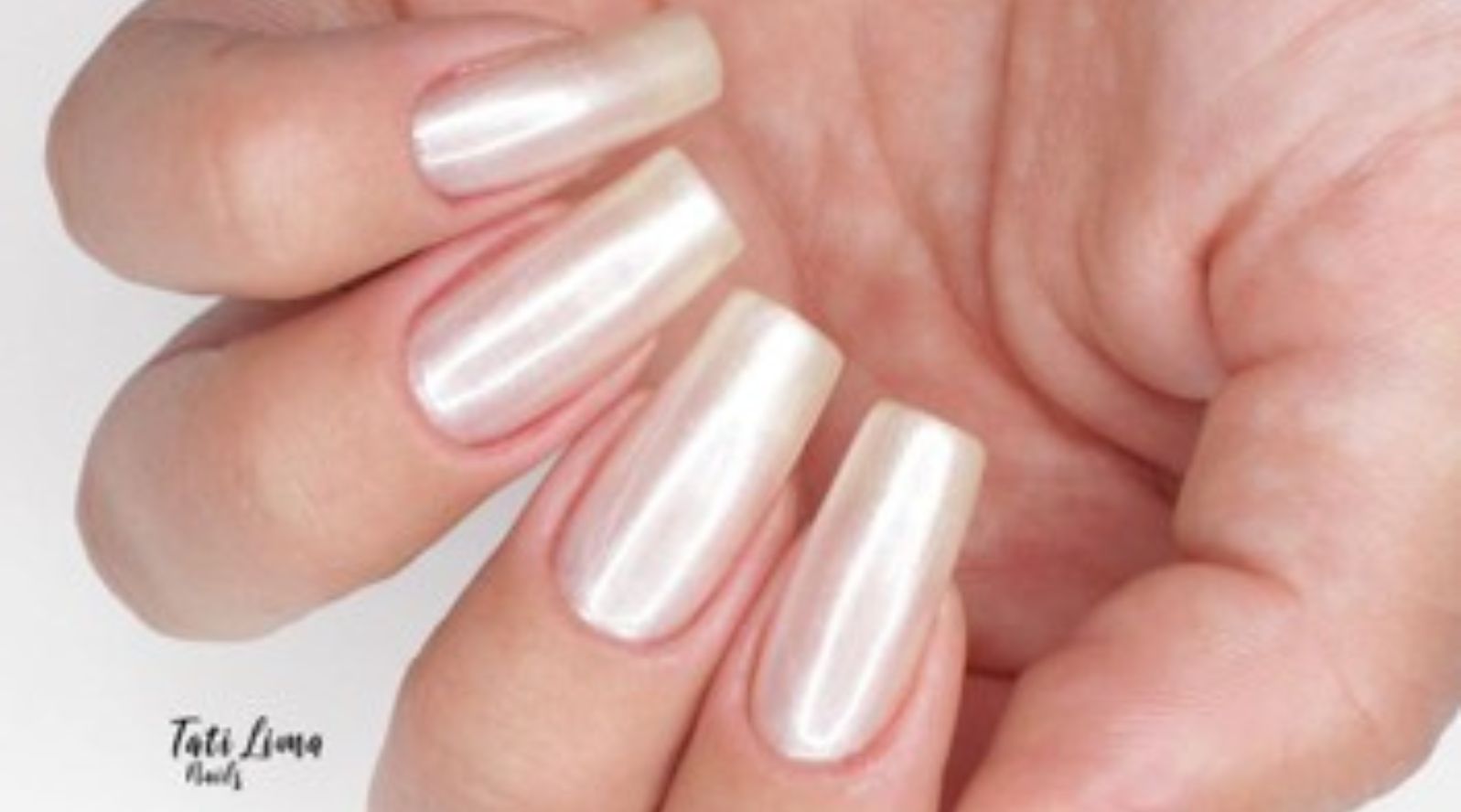 Mão com unhas longas no formato caixão com acabamento perolado e efeito aura em tom branco champanhe com reflexo metálico.