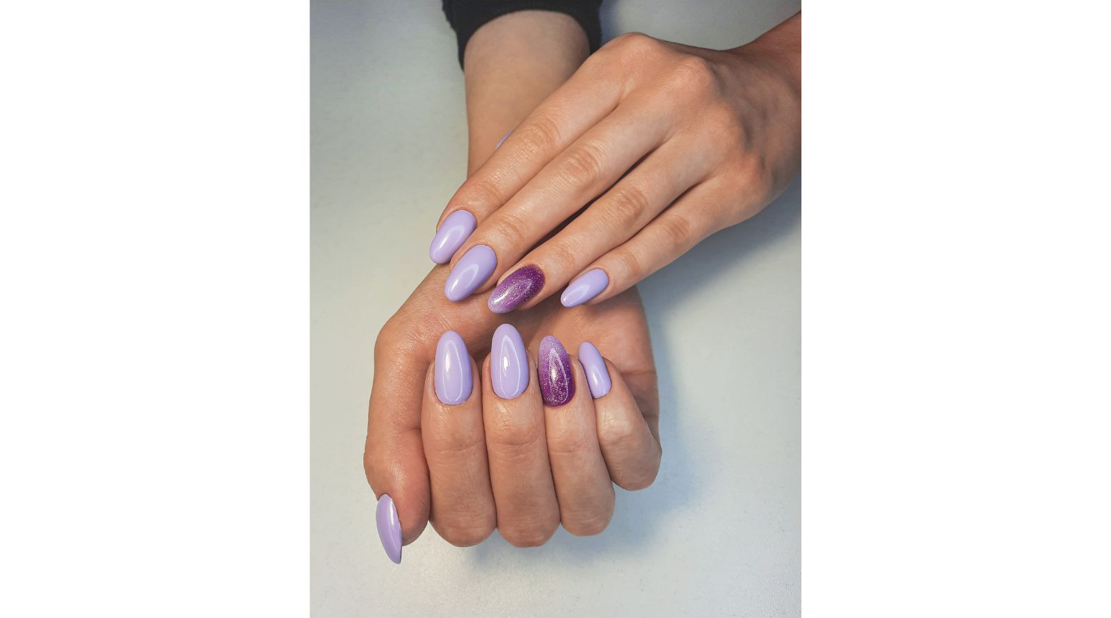 Unhas pintadas de lilás e degrade com brilho na unha do dedo anelar.
