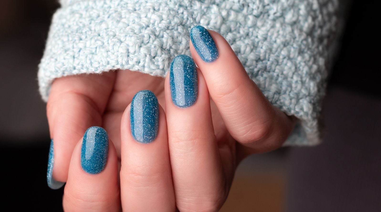 Mãos com unha com glitter azul turquesa, efeito cintilante nas unhas médias e formato oval.