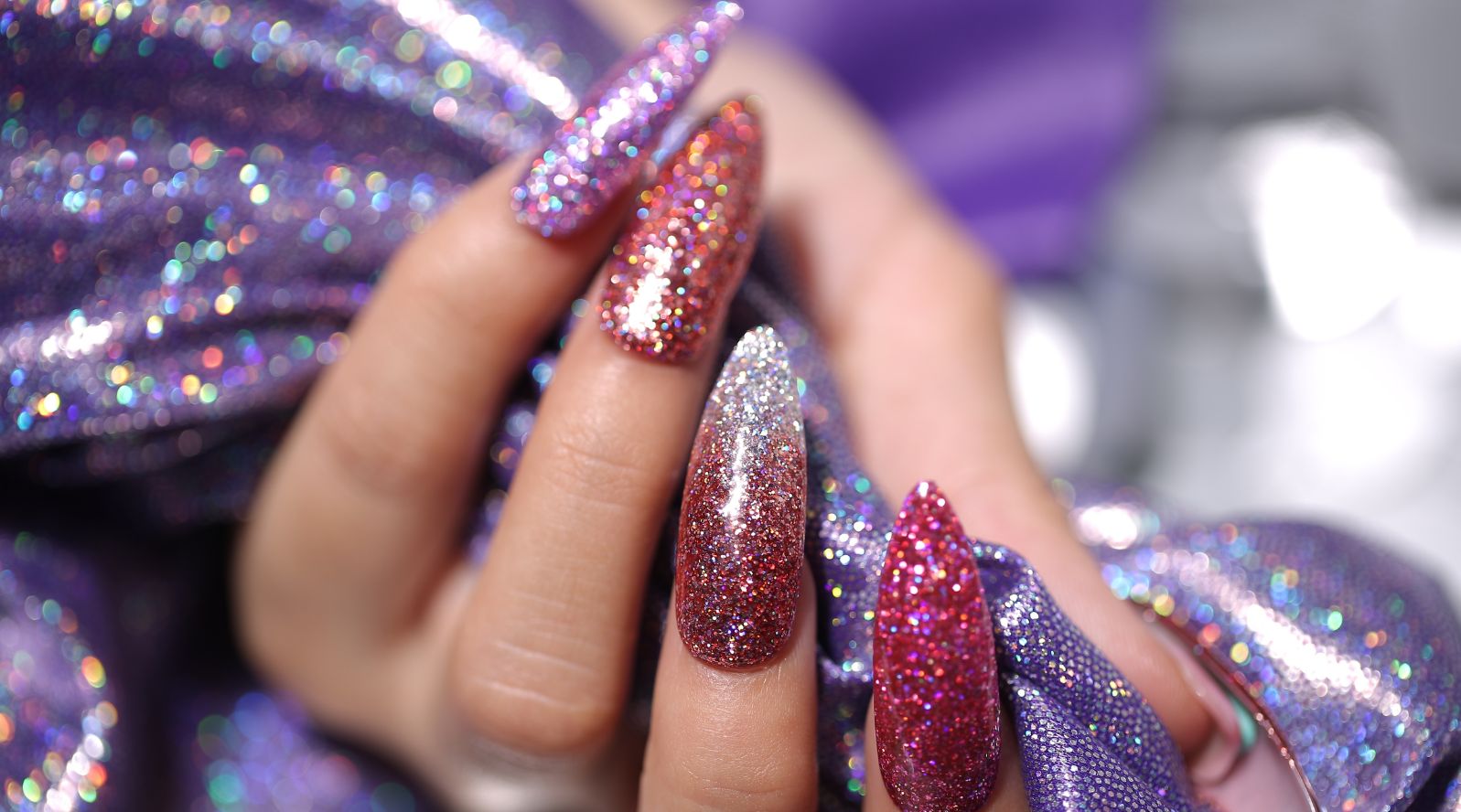 Mãos com unhas longas e esmaltação toda em glitter.