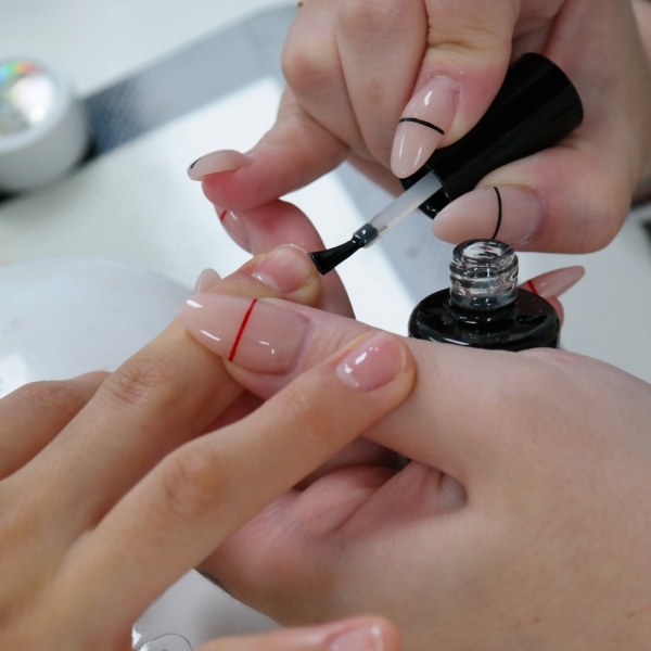Profissional manicure aplica uma base nas unhas de sua cliente e realiza os cuidados para evitar a unha encravada.