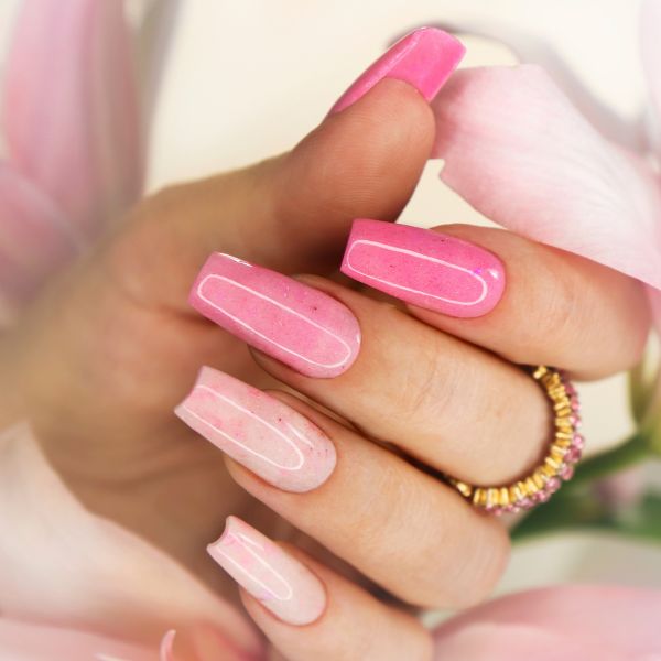 Unha rosa longa e quadrada, com tons variados de rosa, adornada com um anel dourado.