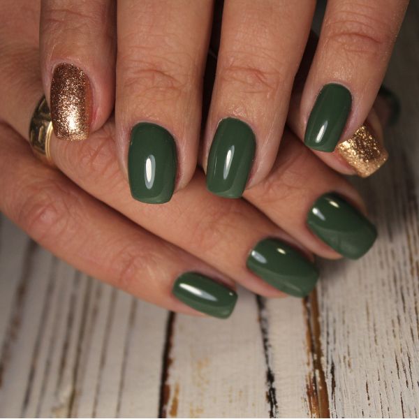 Foto de unhas feitas em esmalte verde escuro, com a filha única estampada com a bandeira do Brasil.