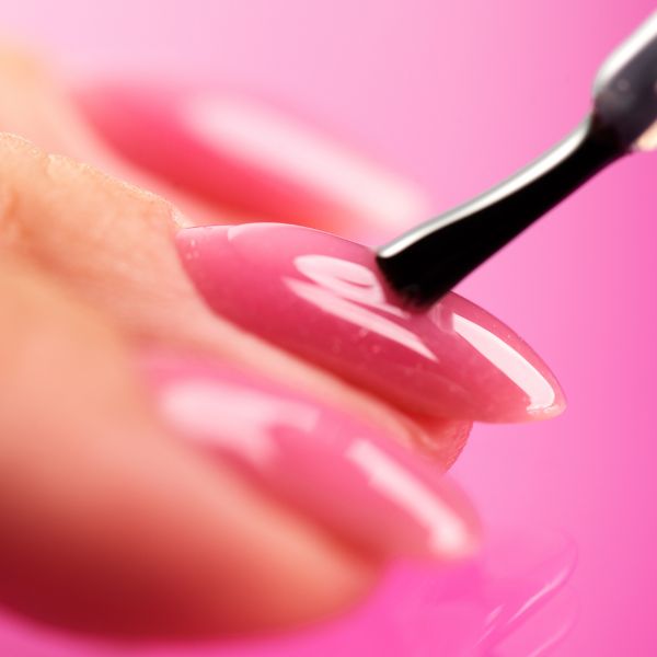 Profissional aplicando o esmalte cor de rosa para criar as unhas decoradas rosa em sua cliente