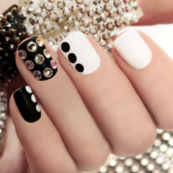 Foto da mão de uma mulher com as unhas decoradas com tons de preto e branco com pedras.