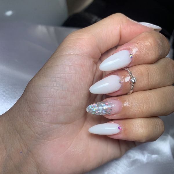 Unhas elegantes longas e pontudas com esmalte prateado com glitter e branco.