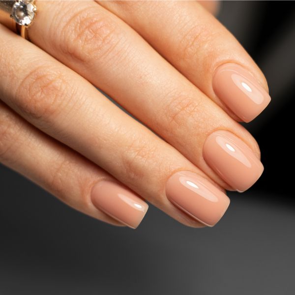Unhas elegantes curtas e quadradas em tom nude, com um anel dourado no dedo anelar.