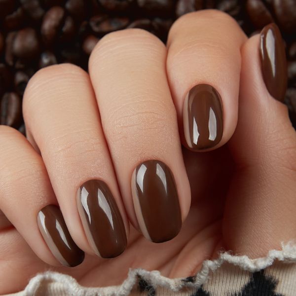 Foto de unhas feitas em tom de marrom café, com grãos de café ao fundo.