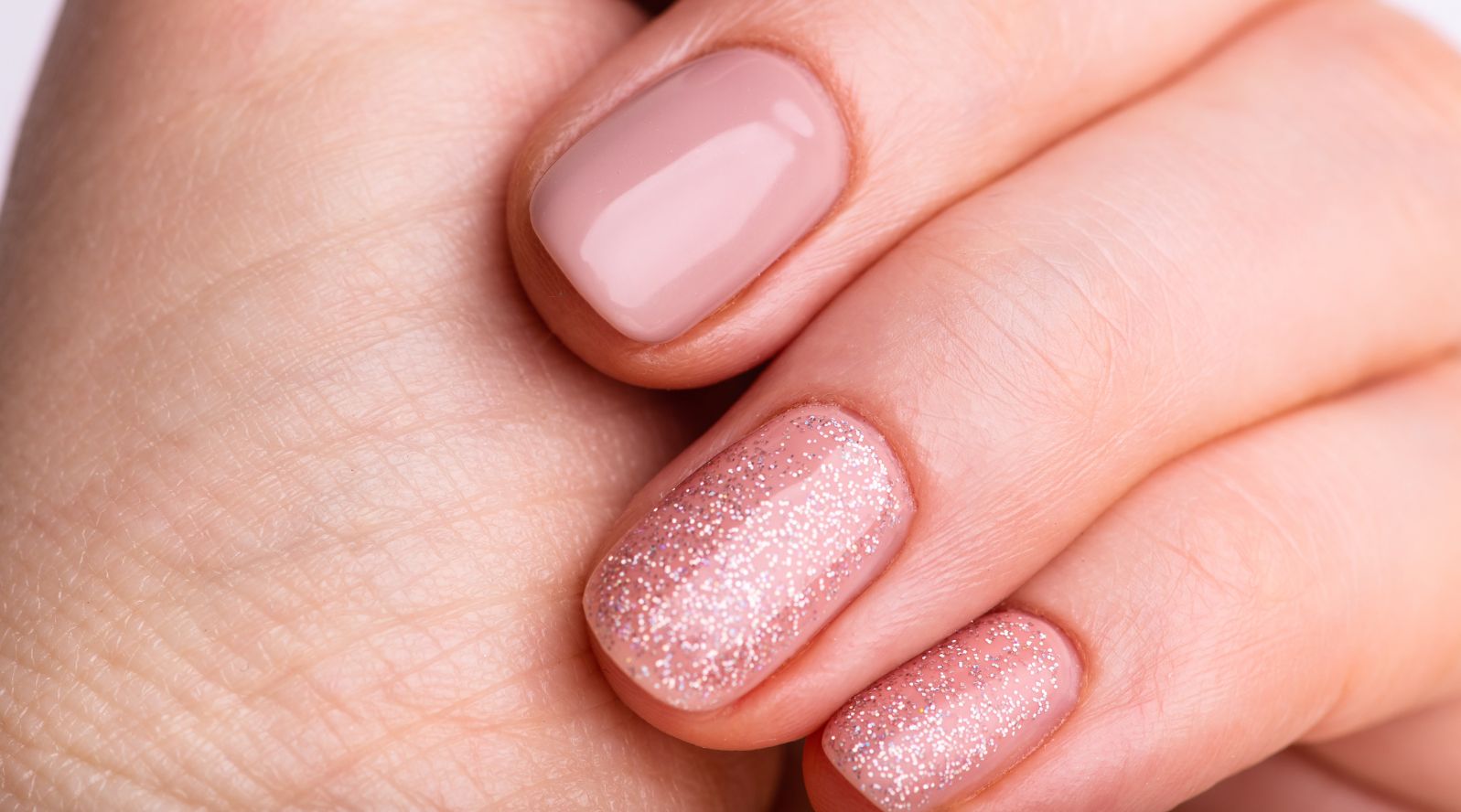 Unhas pintadas na cor nude com o dedo anela e mindinho com uma camada de brilho.