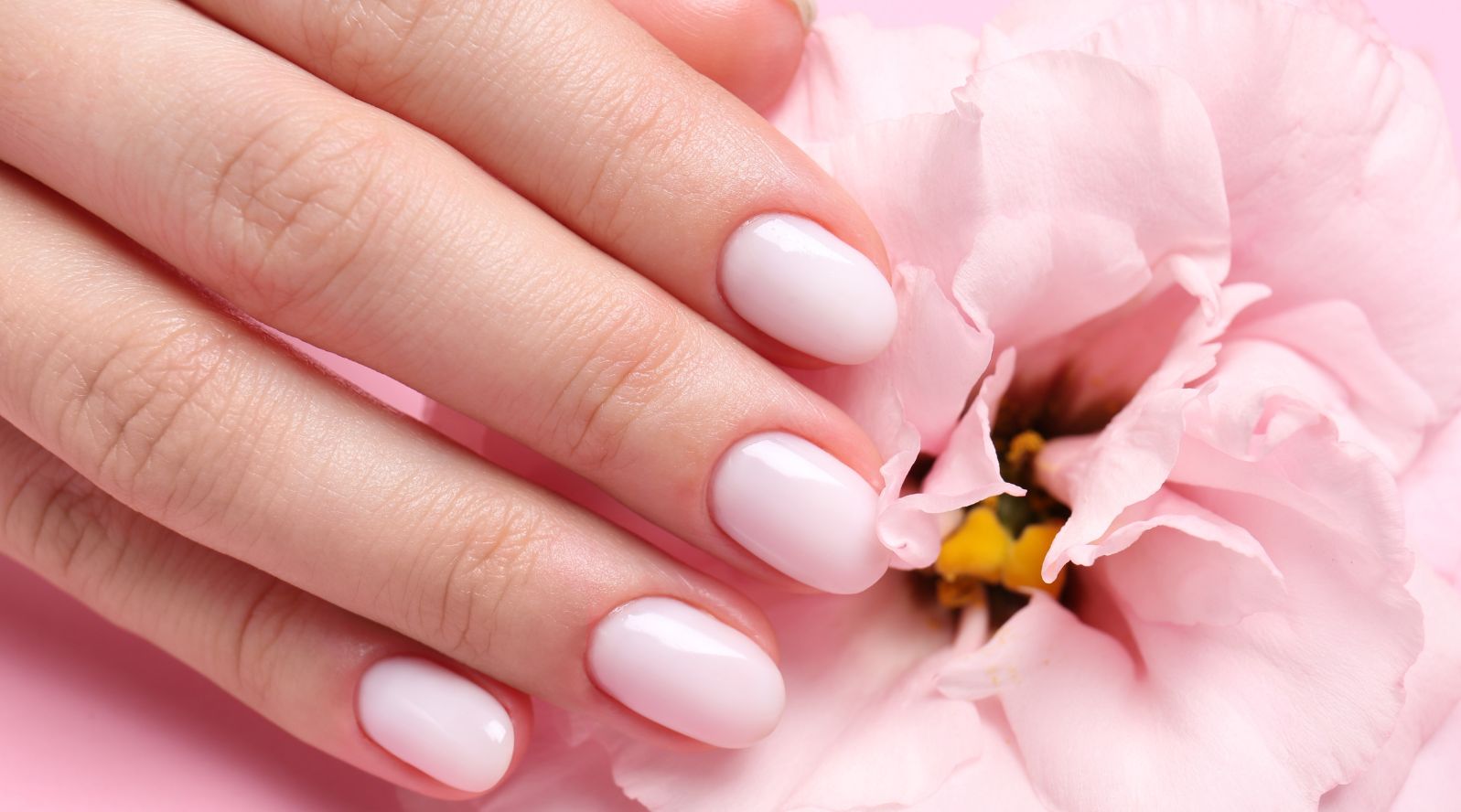 Unhas pintadas de rosa claro com um uma flor na mesma coloração no fundo.