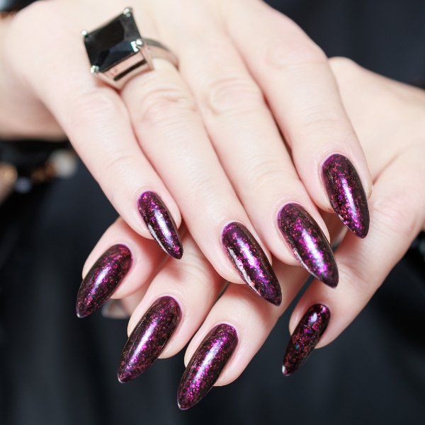 Foto das mãos de uma mulher branca com as unhas decoradas na cor vinho.